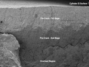 Low magnification SEM image of the inhibited acid cleaned “B” side axial fracture surface. The narrow slits in the fracture surface are sulfide stringers that have been preferentially corroded. The discoloration suggests two stages of crack propagation before rupture.