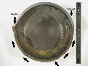 A view of the circumferential fracture at the cylinder bottom revealed after sectioning. The bottom internal surface displays some corrosion (brown staining). The fracture propagation direction is indicated by the arrows.